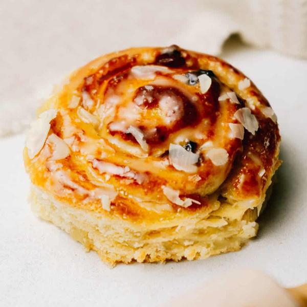 Marzipan Rosinenschnecke ﻿Zart zergehender Plunderteig mit Lübecker Marzipanfüllung und Rosinen, verziert mit Fondant und Mandelblättchen.