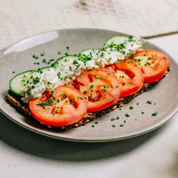 Frühlingsbrot ﻿Korn an Korn mit Joghurtrahmaufstrich Schnittlauch und Petersilie, Gurken- und Tomatenscheiben.